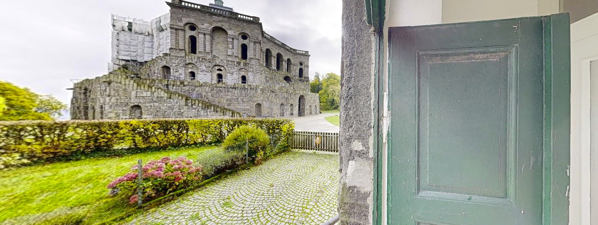 Blick aus der Haustür des Aufseherhauses direkt auf das Herkules-Denkmal. Die Aufnahme zeigt die außergewöhnliche Lage des Gebäudes im UNESC "Blick aus der Haustür des Aufseherhauses am Herkules auf das UNESCO-Herkulesdenkmal im Bergpark Wilhelmshöhe."